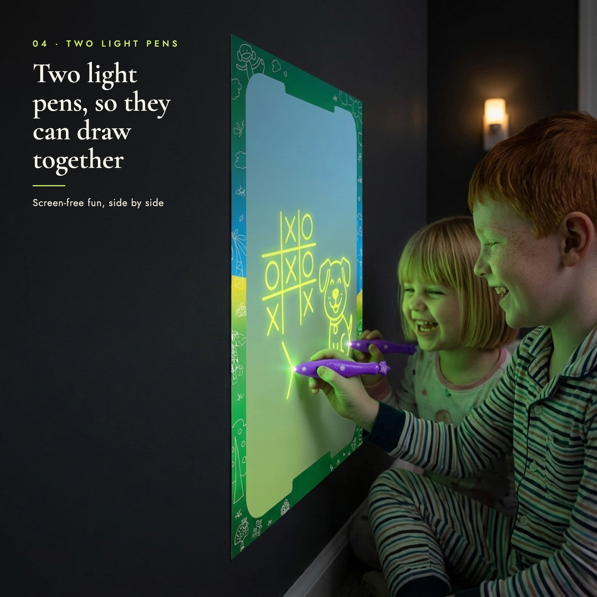 Two children drawing together on the glowing canvas in a dark playroom