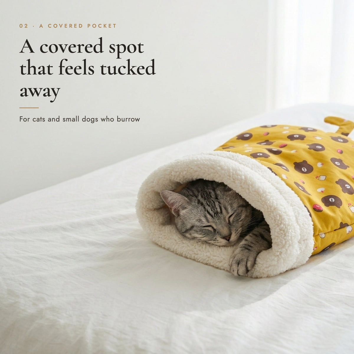 Grey cat sleeping inside a Honey Bear print pet sleeping bag on a bed
